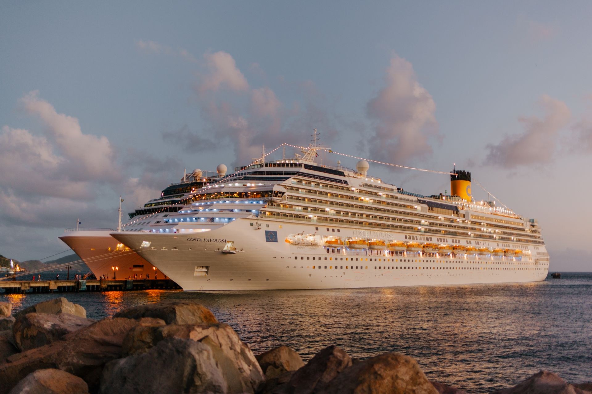 Large white cruise ship docked at port at dusk, deck lights glowing