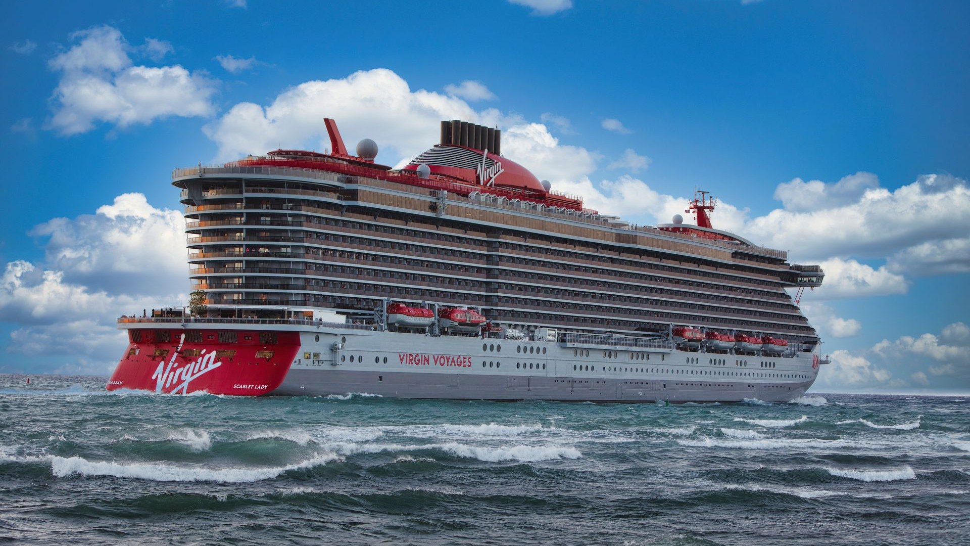 Virgin Voyages' Scarlet Lady cruise ship sailing through open ocean waters under a clear blue sky
